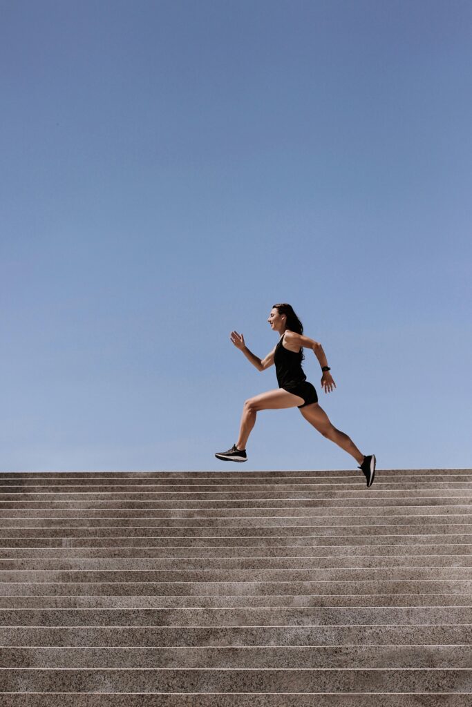 pexels-photo-4422913-4422913 Athletic woman sprinting up outdoor stairs under clear blue sky, showcasing fitness and strength.